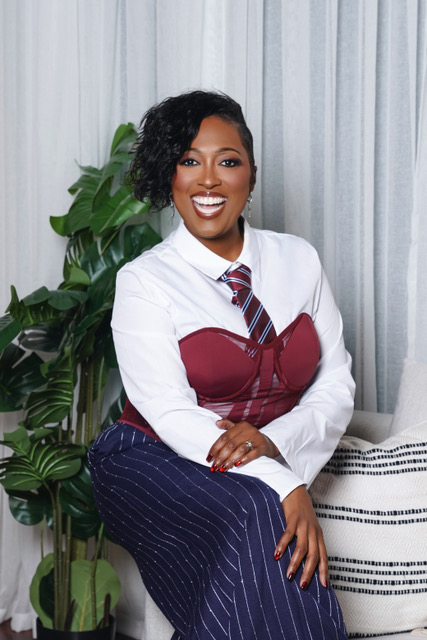 Dr. Mia Young smiling, seated in a white shirt, burgundy corset, and striped tie
